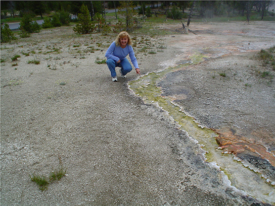 The photo shows a woman squatting next to a stream of green-colored water.