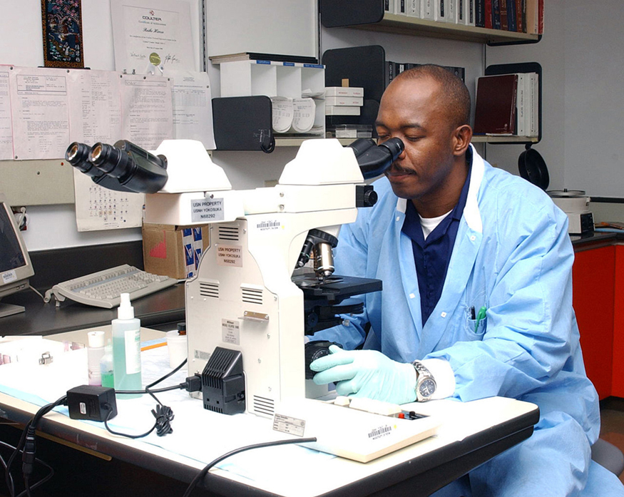 Image of a man viewing through the ocular lens and with his hand on the fine adjustment of the microscope.