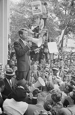 A photograph shows Robert Kennedy speaking to a large crowd through a megaphone.