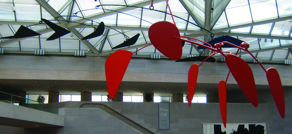 An image of a calder mobile is shown. It has several black and red geometric shapes hanging down.