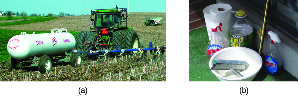 This photograph shows a large agricultural tractor in a field pulling a field sprayer and a large, white cylindrical tank which is labeled “Caution Ammonia.”