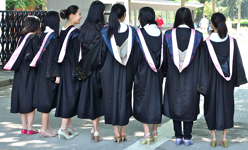 Eight girls graduating from college in their gowns, with their backs turned toward the camera