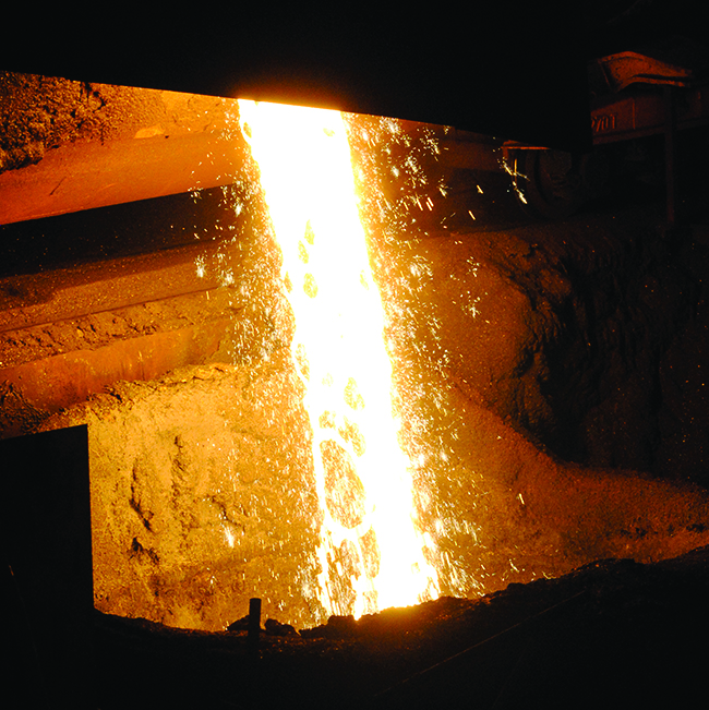 This figure shows a photo of molten iron. A bright yellow-orange glow appears just left of center in the figure. Smoke appears to be rising toward the top center of the figure. Just below and to the right, sparks appear to be falling.