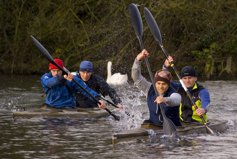 Four men racing up a river in their kayaks.