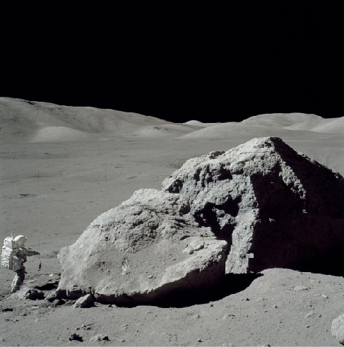 Scientist on the Moon. Photograph of geologist Harrison Schmitt collecting samples near a large boulder on the Lunar surface. Schmitt is at lower left, dwarfed by the massive boulder.