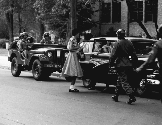 An image of several armed military officers escorting two people out of a car.