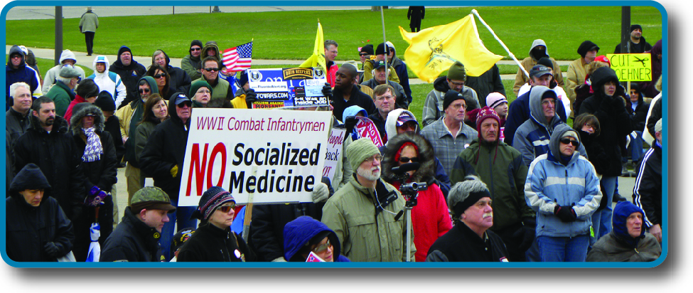 An image of a crowd of people holding signs and flags. One sign reads “WWII Combat Infantrymen No Socialized Medicine”.