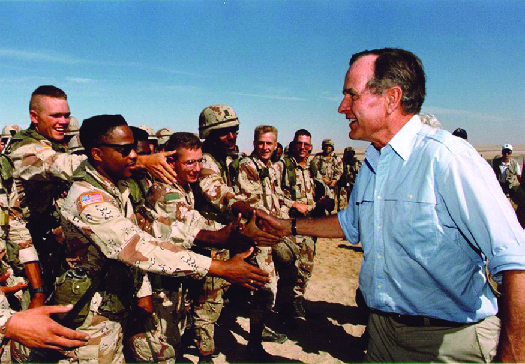 George H. W. Bush shaking hands with U.S. troops outdoors.