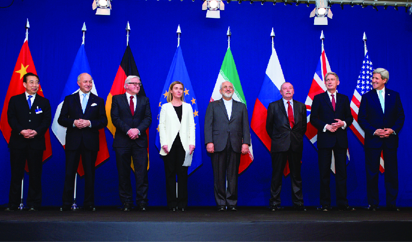 An image of the ministers of foreign affairs and other officials standing on a stage, each in front of the flag of their country.