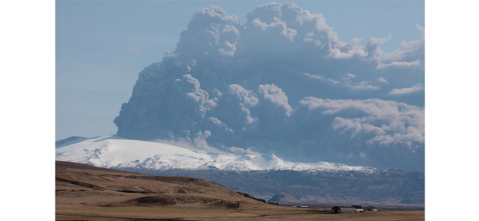 A photograph of an erupting volcano. A giant plume of gas and dust can be seen being ejected from it.