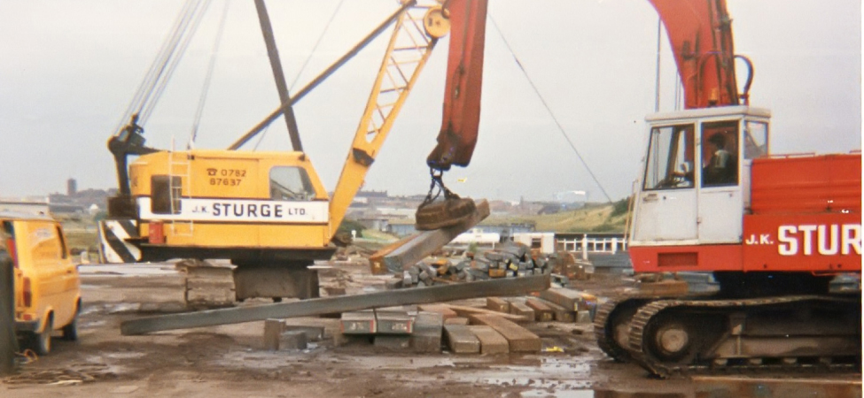 A photo of steel beams being lifted by an electromagnet at a construction site